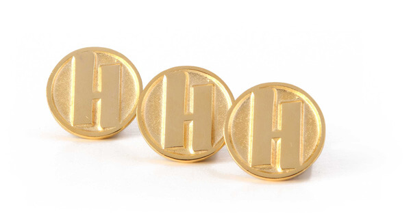 Gold circular pins with a branded logo with the letter H